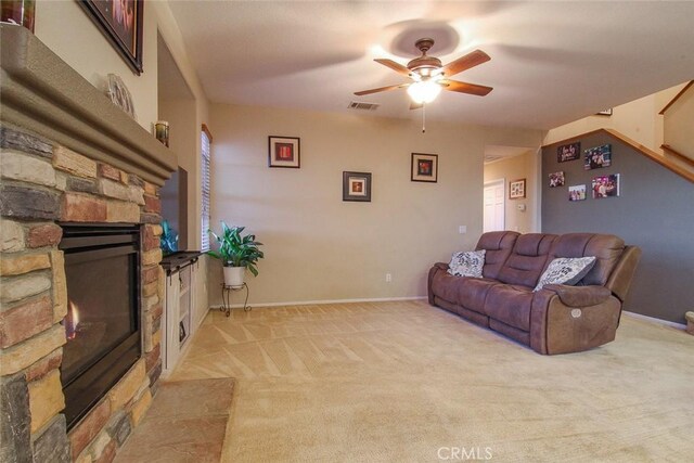 carpeted living room with a stone fireplace and ceiling fan
