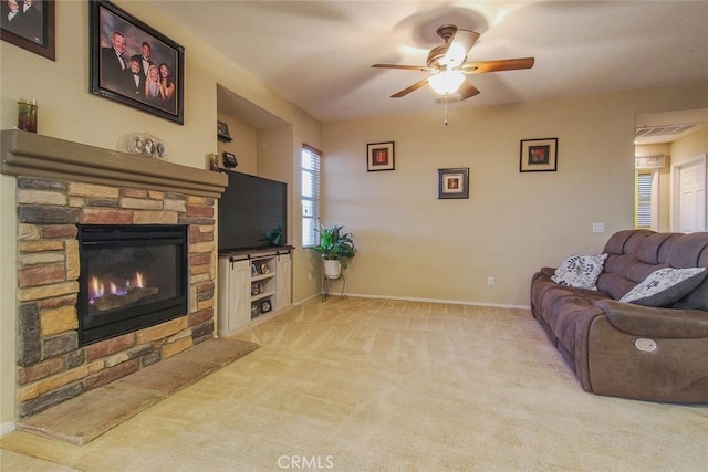 living room featuring ceiling fan, light colored carpet, and a stone fireplace