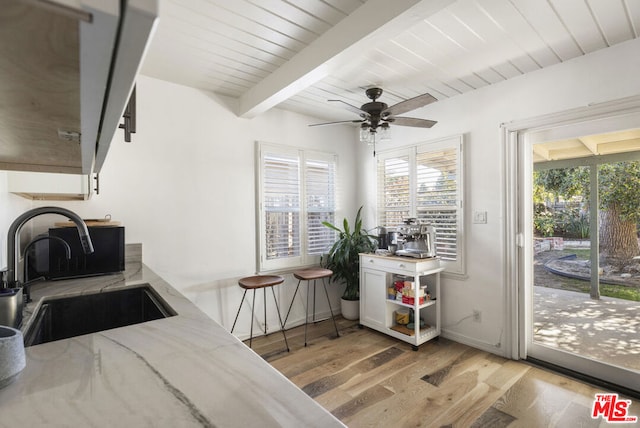 kitchen with white cabinetry, beamed ceiling, light hardwood / wood-style floors, sink, and ceiling fan