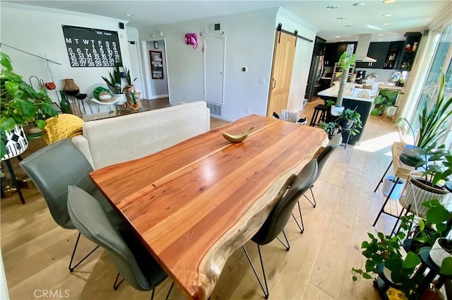 dining space with ornamental molding, a barn door, and light hardwood / wood-style flooring