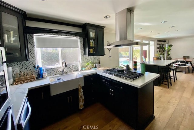 kitchen with sink, island range hood, light wood-type flooring, kitchen peninsula, and stainless steel gas stovetop