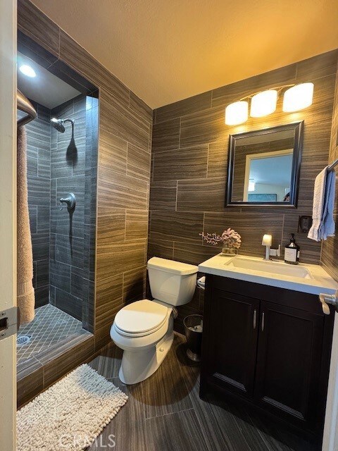 bathroom featuring tiled shower, vanity, toilet, and tile walls