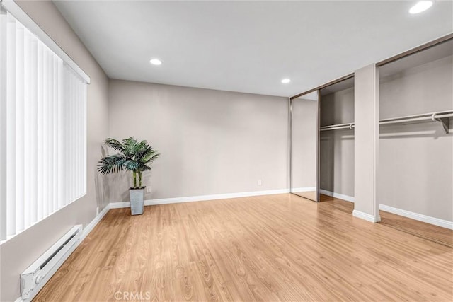 unfurnished bedroom with baseboard heating, multiple closets, and light hardwood / wood-style flooring