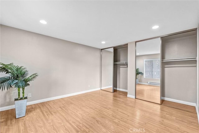 unfurnished bedroom with multiple closets, a baseboard radiator, and light wood-type flooring