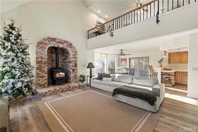 living room with hardwood / wood-style flooring, ceiling fan, a wood stove, and a high ceiling