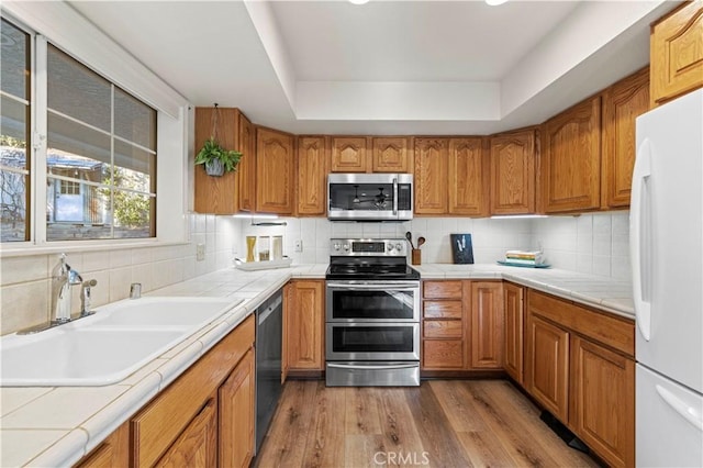 kitchen featuring tile countertops, hardwood / wood-style floors, decorative backsplash, sink, and stainless steel appliances