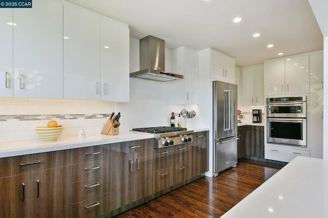 kitchen with dark wood-type flooring, wall chimney exhaust hood, white cabinetry, appliances with stainless steel finishes, and decorative backsplash