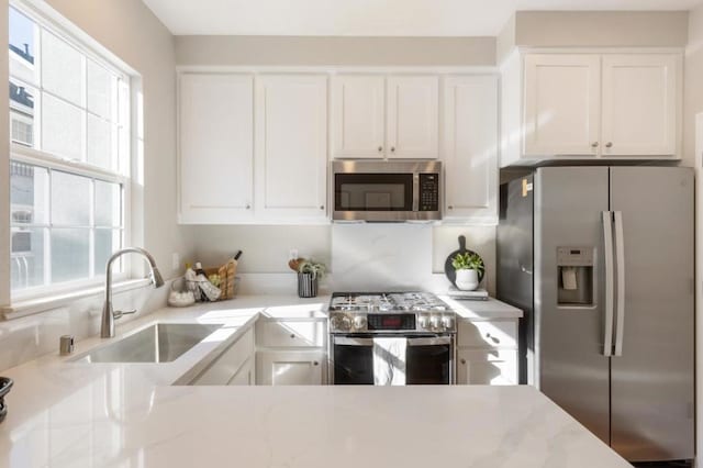 kitchen with white cabinetry, sink, light stone counters, and appliances with stainless steel finishes