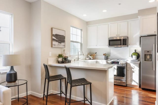 kitchen with white cabinetry, appliances with stainless steel finishes, a kitchen breakfast bar, kitchen peninsula, and hardwood / wood-style floors