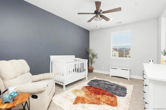 bedroom featuring ceiling fan, light carpet, and a crib