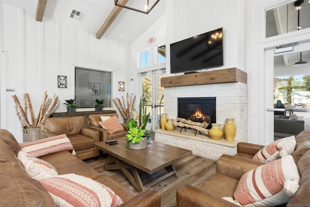 living room featuring wood-type flooring, beam ceiling, a fireplace, and a high ceiling