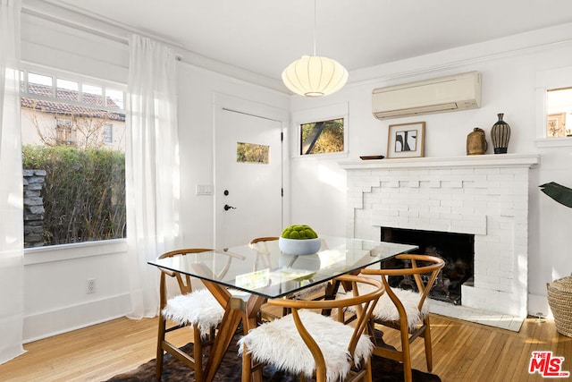 dining space with a brick fireplace, hardwood / wood-style floors, a wall mounted air conditioner, and a wealth of natural light