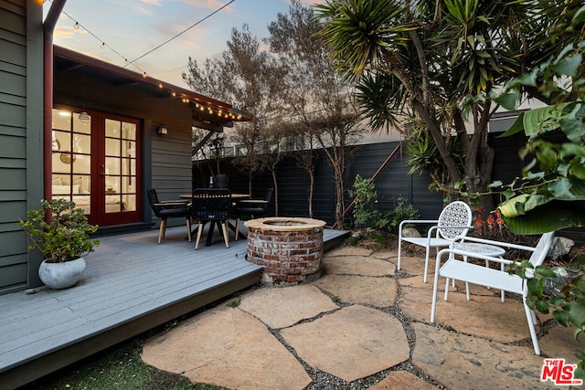 patio terrace at dusk with a deck, an outdoor fire pit, and french doors