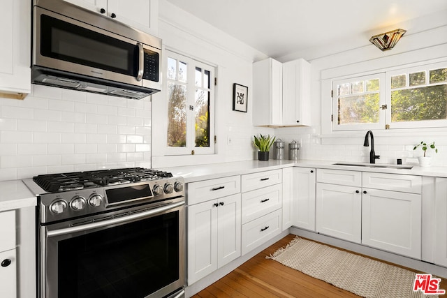 kitchen with appliances with stainless steel finishes, white cabinetry, decorative backsplash, sink, and light hardwood / wood-style flooring