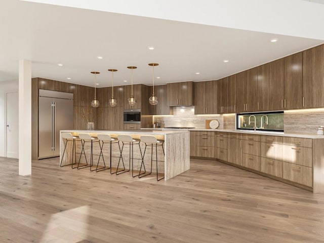 kitchen with stainless steel appliances, a spacious island, light hardwood / wood-style floors, and hanging light fixtures