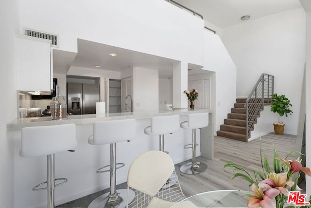 kitchen with light hardwood / wood-style floors, kitchen peninsula, stainless steel fridge, a kitchen breakfast bar, and white cabinets