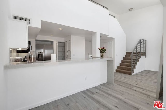 kitchen with kitchen peninsula, white cabinetry, light hardwood / wood-style flooring, and stainless steel fridge