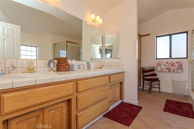 bathroom with a shower with shower door, decorative backsplash, tile patterned floors, vaulted ceiling, and vanity