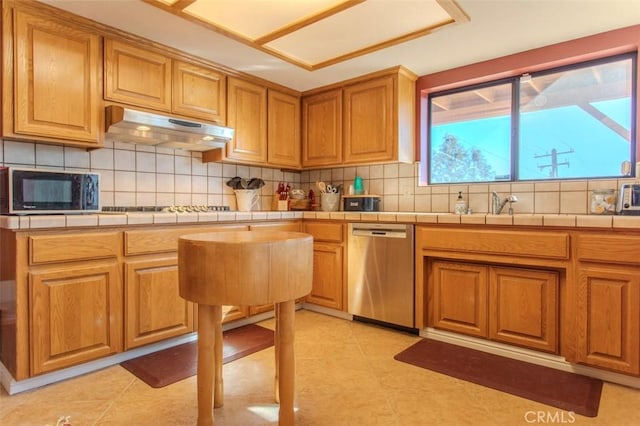 kitchen featuring tile counters, sink, backsplash, cooktop, and stainless steel dishwasher