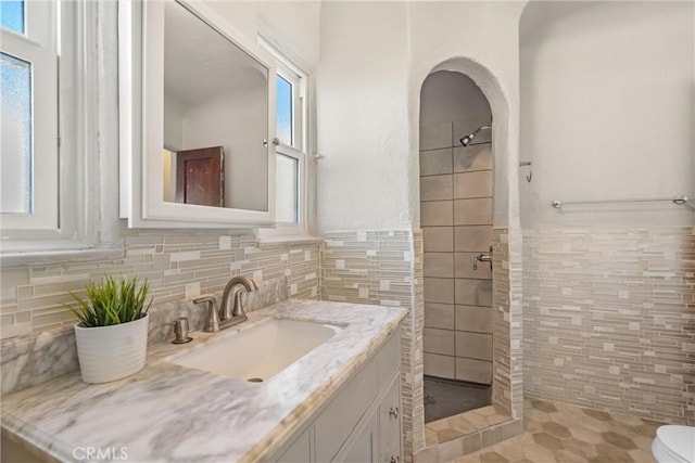 bathroom featuring tiled shower, vanity, toilet, and tile walls