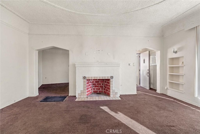 unfurnished living room with a tiled fireplace, dark carpet, built in features, and a textured ceiling