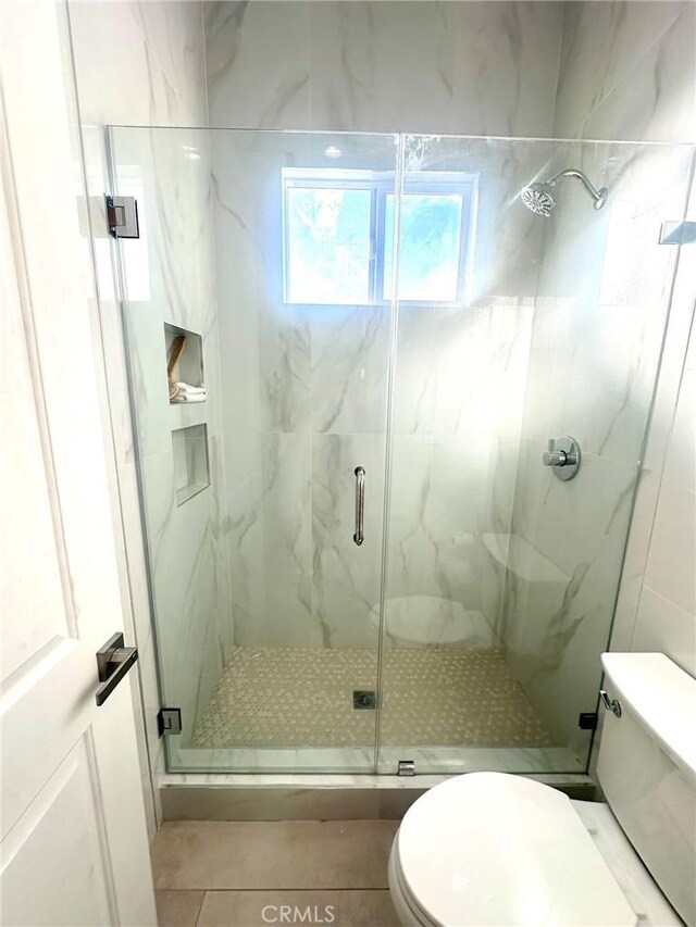 bathroom featuring toilet, tile patterned floors, and a shower with shower door