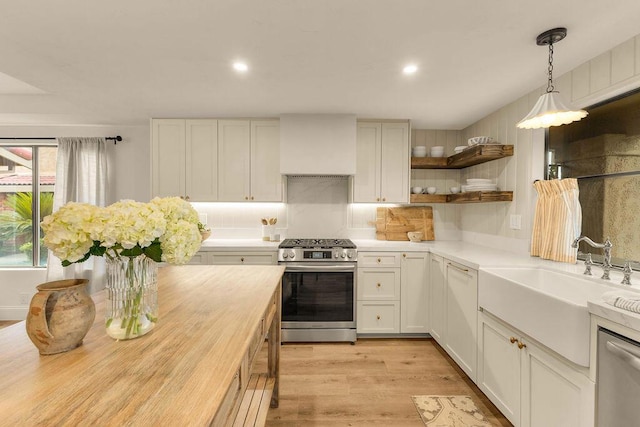 kitchen with sink, light hardwood / wood-style flooring, appliances with stainless steel finishes, white cabinets, and wall chimney exhaust hood