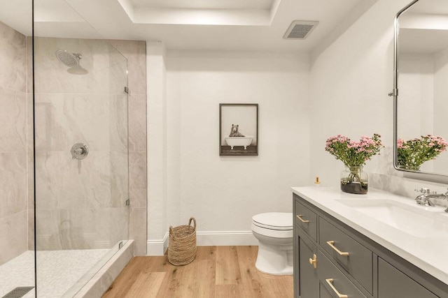 bathroom with toilet, vanity, a tray ceiling, hardwood / wood-style flooring, and a tile shower