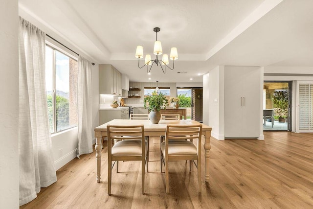 dining room with a raised ceiling, a healthy amount of sunlight, an inviting chandelier, and light hardwood / wood-style floors