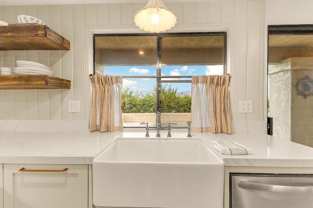 kitchen featuring stainless steel dishwasher, light stone countertops, wooden walls, and white cabinetry