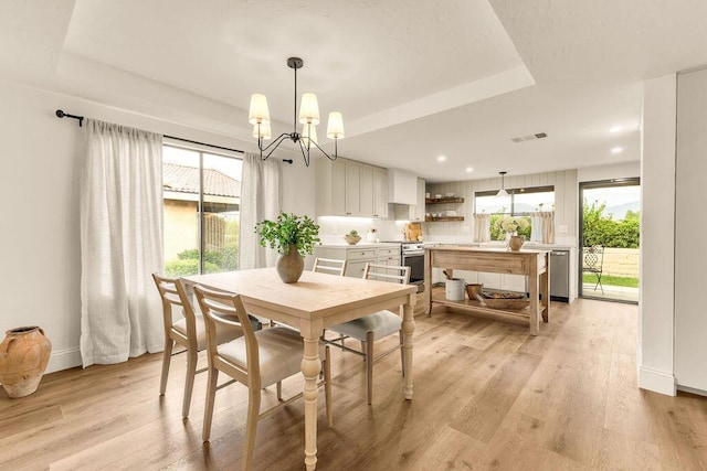 dining room featuring light hardwood / wood-style floors, a raised ceiling, a chandelier, and a healthy amount of sunlight