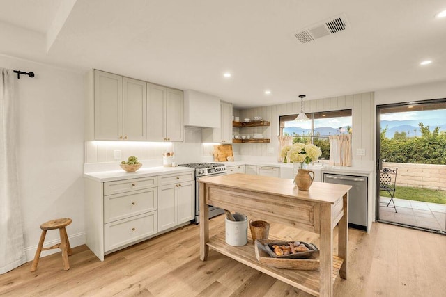 kitchen with decorative light fixtures, white cabinetry, stainless steel appliances, tasteful backsplash, and light hardwood / wood-style flooring