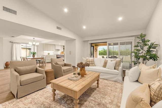 living room with vaulted ceiling, an inviting chandelier, and light hardwood / wood-style floors