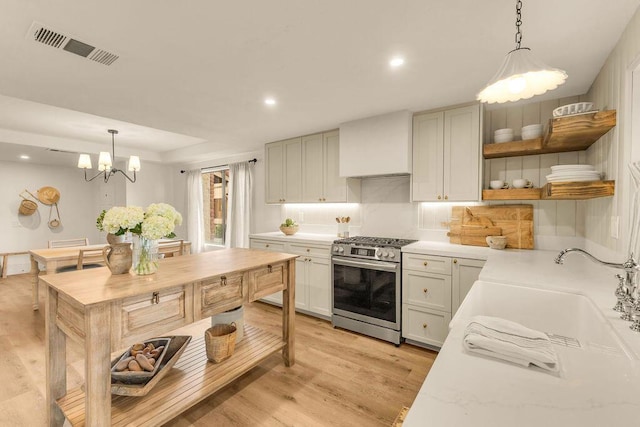 kitchen with pendant lighting, wall chimney exhaust hood, gas stove, light hardwood / wood-style floors, and sink