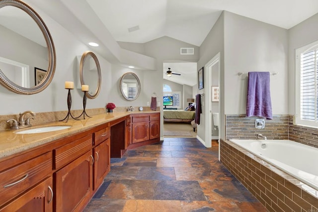 bathroom featuring lofted ceiling, ceiling fan, vanity, a relaxing tiled tub, and toilet