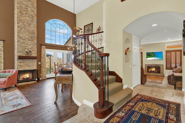 stairway featuring a towering ceiling, wood-type flooring, and a stone fireplace