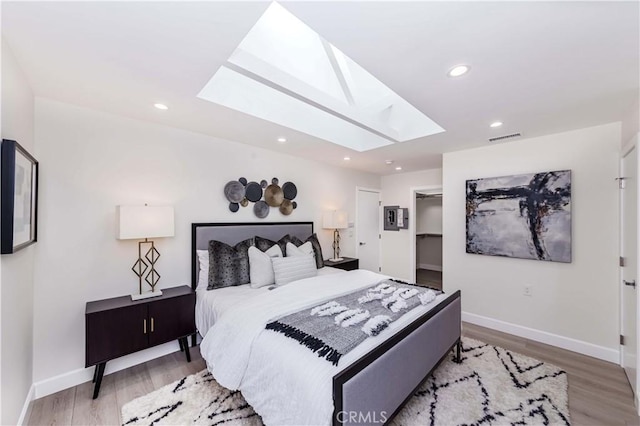 bedroom featuring a walk in closet, light wood-type flooring, and a skylight