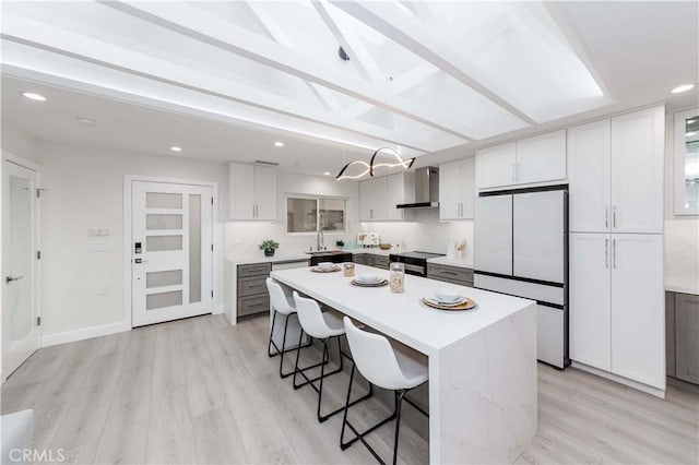 kitchen featuring wall chimney exhaust hood, hanging light fixtures, white refrigerator, gray cabinets, and a kitchen island