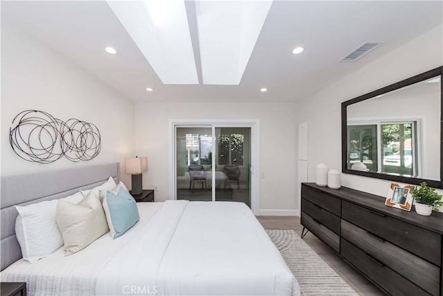 bedroom featuring access to exterior, a skylight, and hardwood / wood-style floors