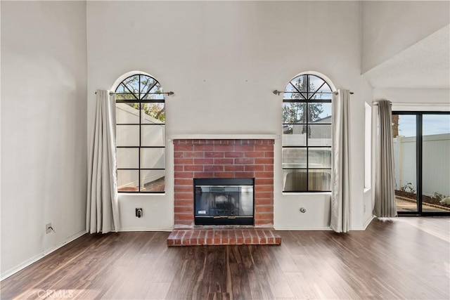 unfurnished living room with a brick fireplace, a wealth of natural light, wood-type flooring, and a high ceiling