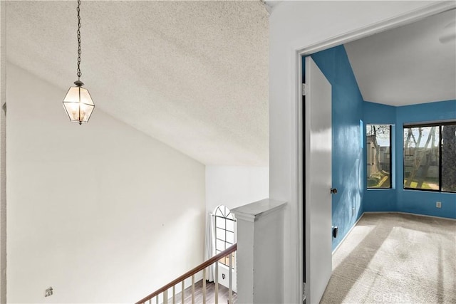 hall featuring a textured ceiling, lofted ceiling, and light colored carpet