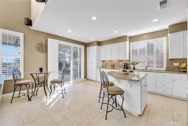 kitchen featuring plenty of natural light, white cabinetry, light stone counters, and a center island