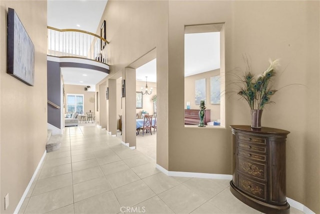 hall featuring light tile patterned floors, a towering ceiling, and an inviting chandelier