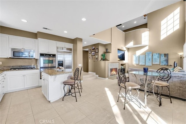 kitchen with light stone counters, white cabinetry, appliances with stainless steel finishes, and a kitchen bar