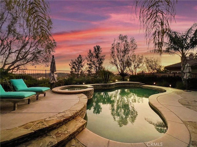 pool at dusk with an in ground hot tub and a patio