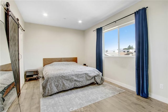 bedroom with a barn door and light hardwood / wood-style flooring