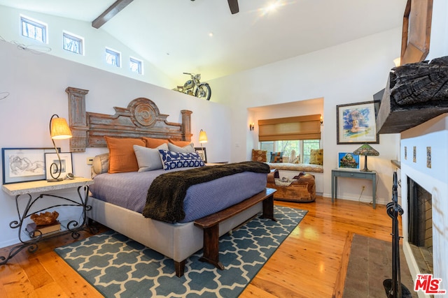 bedroom with lofted ceiling with beams, a tile fireplace, and hardwood / wood-style flooring