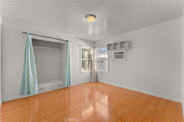 unfurnished bedroom with an AC wall unit, wood-type flooring, and a closet