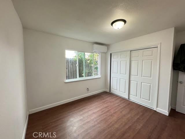 unfurnished bedroom featuring an AC wall unit, dark hardwood / wood-style flooring, and a closet