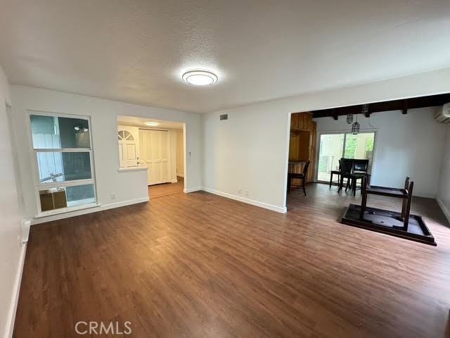 unfurnished living room with hardwood / wood-style flooring, a wall unit AC, and a textured ceiling